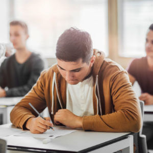 Schüler schreibt konzentriert die Prüfung B1 telc im Klassenzimmer, offizieller Deutschtest für Mittelstufenniveau.