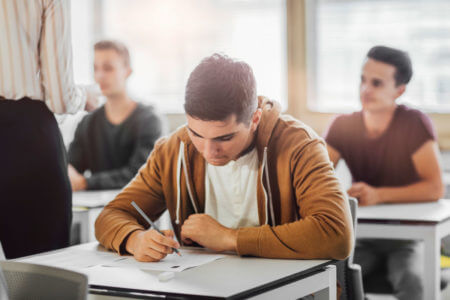 Sch&uuml;ler schreibt konzentriert die Pr&uuml;fung B1 telc im Klassenzimmer, offizieller Deutschtest f&uuml;r Mittelstufenniveau.