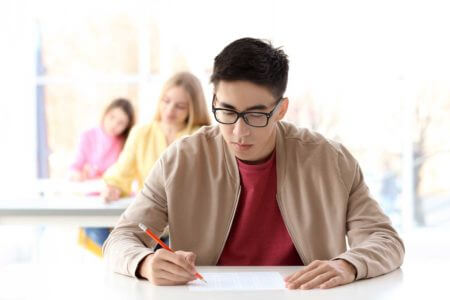 Student schreibt konzentriert die Deutschpr&uuml;fung C1 Hochschule, offizieller Sprachtest f&uuml;r den Universit&auml;tszugang in Deutschland.