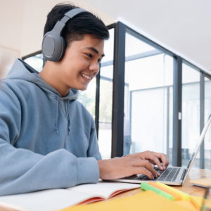 Schüler bereitet sich am Laptop mit Kopfhörern auf einen Aufnahmetest vor und macht Notizen für die Prüfungsvorbereitung.