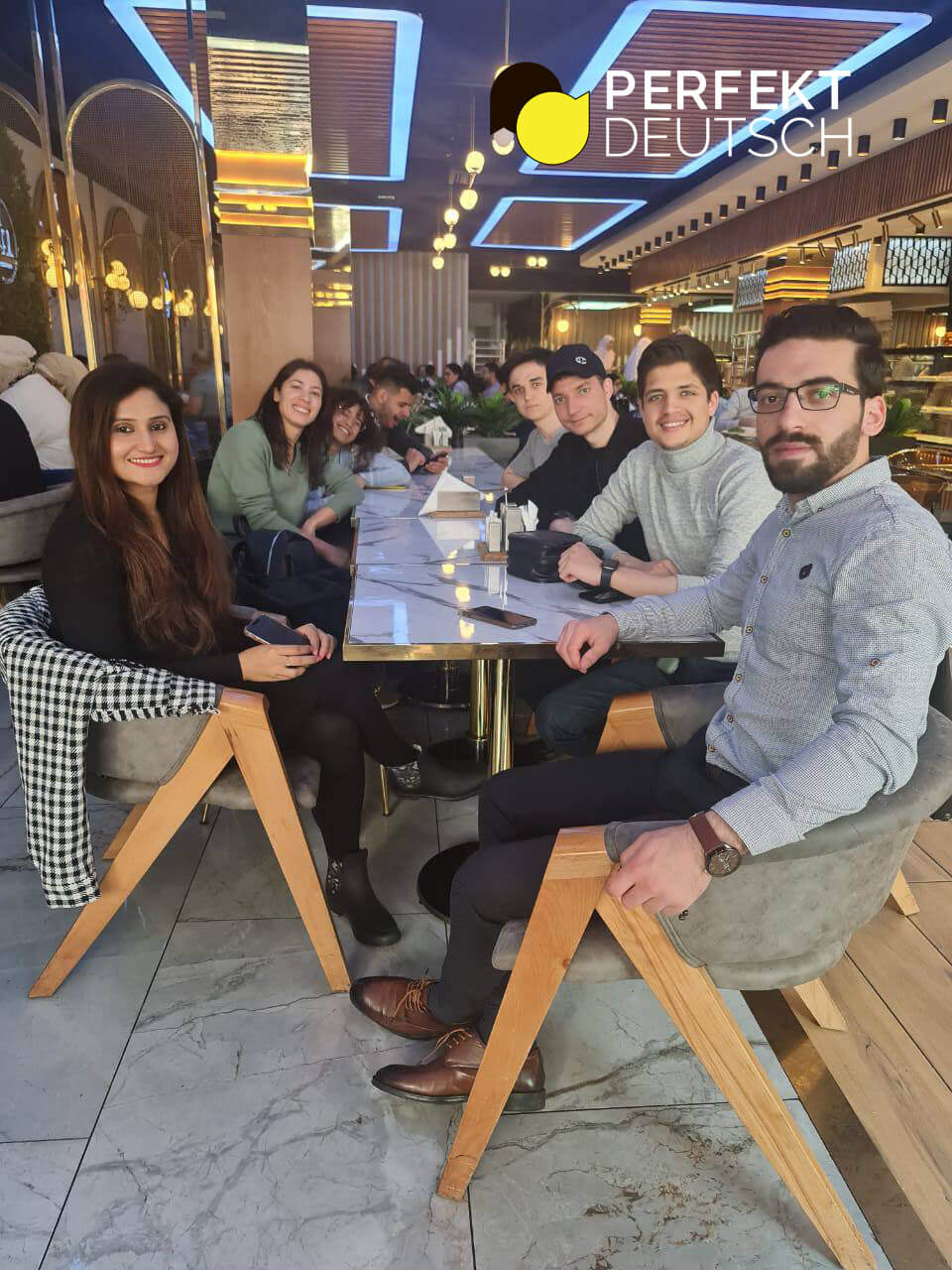 Internationale Gruppe junger Menschen sitzt gemeinsam im Restaurant und pflegt soziale Traditionen in Deutschland durch gemeinsames Beisammensein.